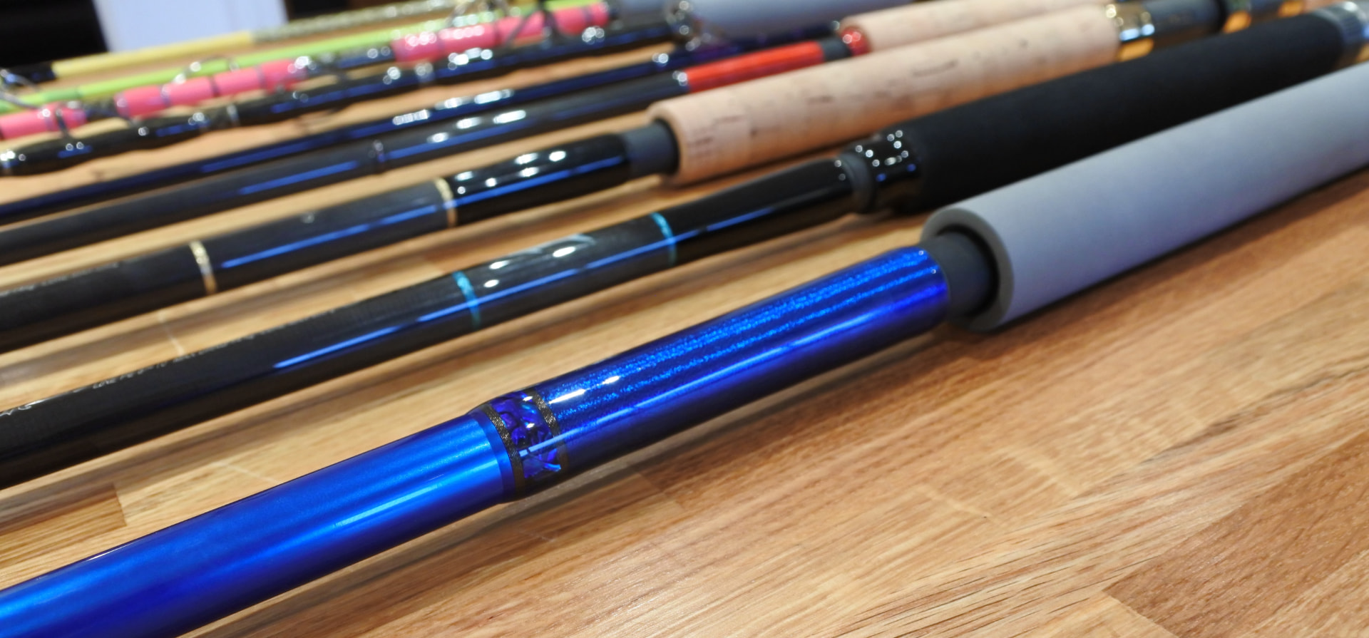 Row of custom rods with colorful thread wraps resting on a wooden bench